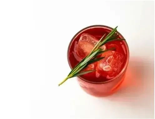 Photograph of a red cocktail in a glass on a white table